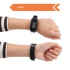 Two hands display a black digital watch with a rectangular screen. The top hand shows the watch face, while the bottom hand shows the buckle side. An orange arrow labeled Details points to the right.