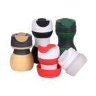 Five colorful plastic cups with lids, each in varying combinations of black, white, green, red, beige, and gray. The cups are stackable, with some placed inside others or positioned upright.