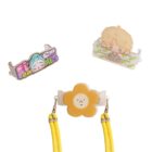 Three colorful phone grips are shown: one with a cartoon of a blue-haired person, another with a cartoon of a blond person, and a yellow flower face with a neutral expression. The grips have yellow straps attached.