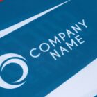 Close-up of a blue and white fabric with the words Company Name and a circular logo printed on it. The design features a wavy pattern in the background.