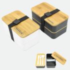 Two stacked bento boxes with bamboo lids and elastic bands. One is white and the other is black. Your Brand Here is engraved on the lids. An open box shows a compartment with utensils.