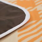 Close-up of a fabric with a brown section bordered by a white trim at the edge. The background has an orange abstract pattern on a light beige surface.
