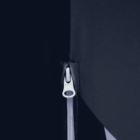 Close-up of a metallic zipper partially closed, set against a dark fabric with a minimalist and abstract composition. The zipper is centrally placed, reflecting a sleek design with contrasting light and dark areas.