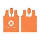 Two orange reusable shopping bags with a white geometric logo and the text REAL ESTATE on one. Both have matching foldable pouches attached at the top.