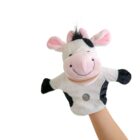 A plush cow hand puppet with a pink nose and ears, black spots, and a smiling face is held up against a plain white background. It is being held by a single hand, visible from the wrist down.