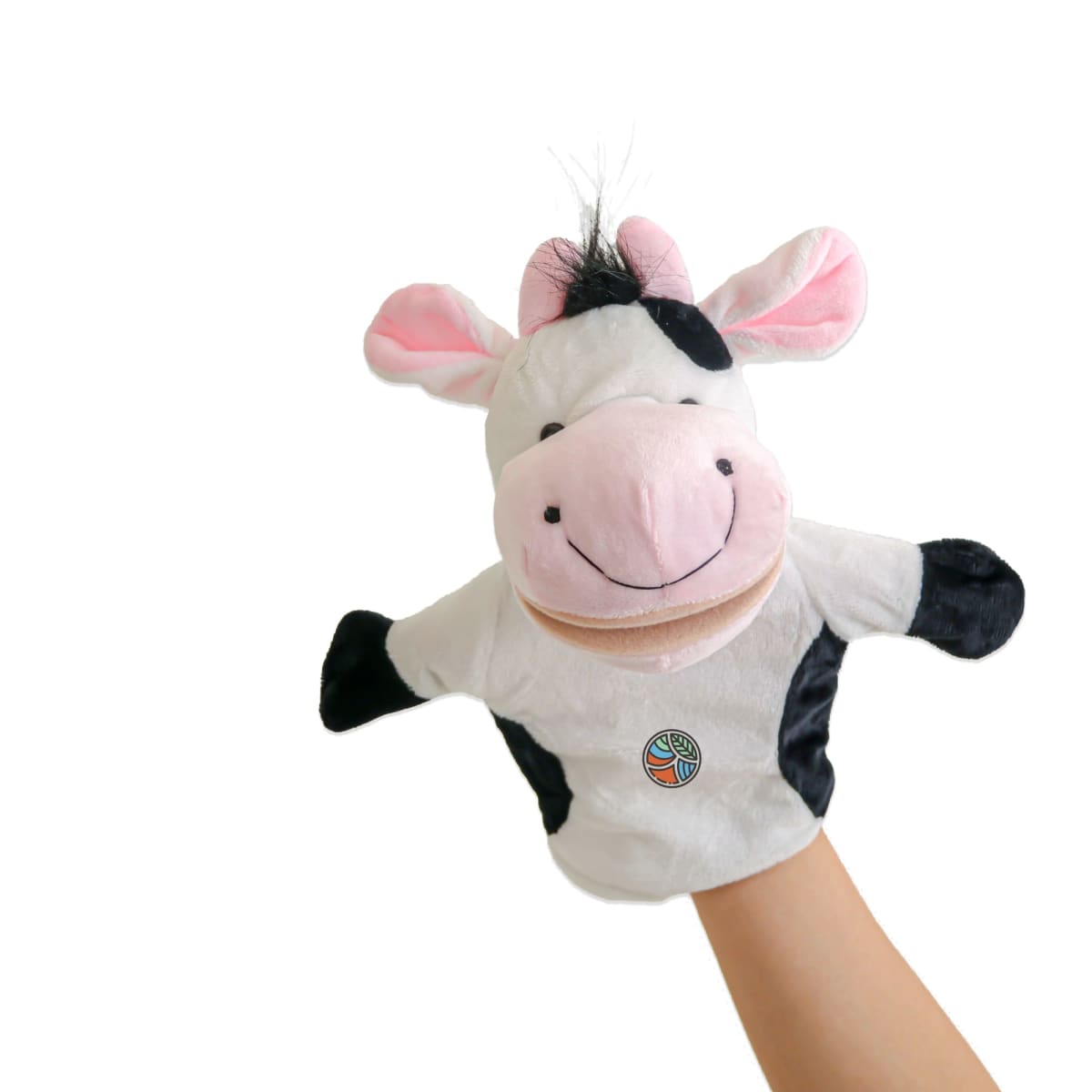 A plush cow hand puppet with a pink nose and ears, black spots, and a smiling face is held up against a plain white background. It is being held by a single hand, visible from the wrist down.