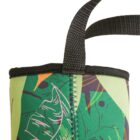 Close-up of a green fabric bag with a tropical leaf pattern and orange accents. The bag has a black woven handle and visible stitching along the side.
