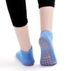A person wearing black leggings is shown from the calves down, sporting blue socks with orange non-slip grips on the soles. They are standing on a white surface.