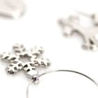 Close-up of shiny silver Christmas-themed ornaments on a white surface. Visible are a snowflake, a reindeer, and other abstract shapes. The focus is on the snowflake, with the reindeer slightly blurred in the background.