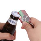 A person uses a metal bottle opener attached to a keychain to open a capped bottle of Belgian wheat beer. The bottle opener features a design of a dogs face and the word Dikke.