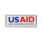 A rectangular badge featuring the text USAID in bold blue and red capital letters. Below, in smaller blue letters, it reads FROM THE AMERICAN PEOPLE. The background is white, and the edges of the badge are black.
