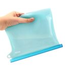 A hand holding a translucent blue silicone food storage bag with a blue seal at the top, set against a plain white background.