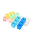 A transparent plastic pill box with four removable compartments. Each compartment is labeled with a day and time: DAY MORN, NOON, or NIGHT. Colors include yellow, green, and blue. The box is open and empty.