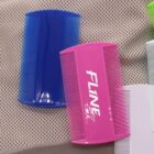 A blue comb and a pink comb with the word FLINE on it are placed on a textured surface. The background includes other partially visible combs in green and white.