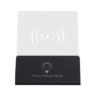 A small black and white wireless charging pad with a minimalist design. The circular charging symbol is on the white surface, and the base is labeled Advertising Media.