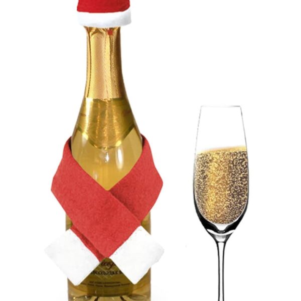 A bottle of champagne is decorated with a red Santa hat and red scarf. Next to it, there is a champagne flute filled with bubbly champagne.
