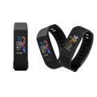Three black fitness trackers with colorful screens displaying time, date, weather, and step count. Two are side by side in a stacked arrangement, and one is standing upright, showcasing the devices flexible strap and modern design.