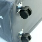 Close-up of a gray fabric suitcase corner, showing two black wheels on metal brackets.