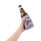 A hand holds a brown glass beer bottle with a blue cap, wrapped in a gray foam koozie featuring the Delta logo and contact information. The koozie has purple and green accents. The background is plain white.