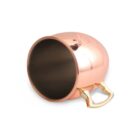 A shiny copper mug with a brass handle, placed on its side against a plain white background. The mug has a reflective surface, showing some reflections and shadows.