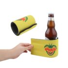 A hand wraps a yellow neoprene bottle holder around a beer bottle. The holder features a logo with a heart, palm trees, and text. Another view shows the holder rolled up, displaying its black interior.