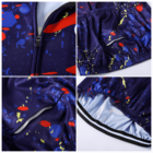 Close-up of a colorful cycling jersey with a splatter pattern in red, blue, and yellow. The image shows four angles, highlighting the fabric texture, a zipper, elastic hems, and a pocket. The interior appears to be lined in light blue.