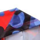 Close-up of a colorful fabric with red, blue, and black abstract patterns featuring curved shapes. Visible red stitching lines at the seam, creating a neat edge. The fabric appears folded, showcasing the inside material partially.