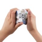 Two hands are holding and twisting a puzzle cube featuring various travel scenes and landmarks on its sides. The cube is partially rotated, suggesting an ongoing attempt to solve it.