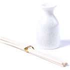 A white ceramic sake bottle with a subtle floral pattern stands next to a bundle of white disposable chopsticks secured with a gold band on a plain white background.