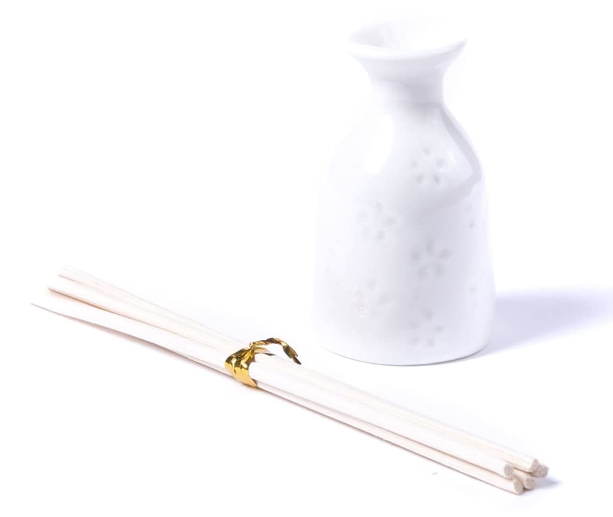 A white ceramic sake bottle with a subtle floral pattern stands next to a bundle of white disposable chopsticks secured with a gold band on a plain white background.
