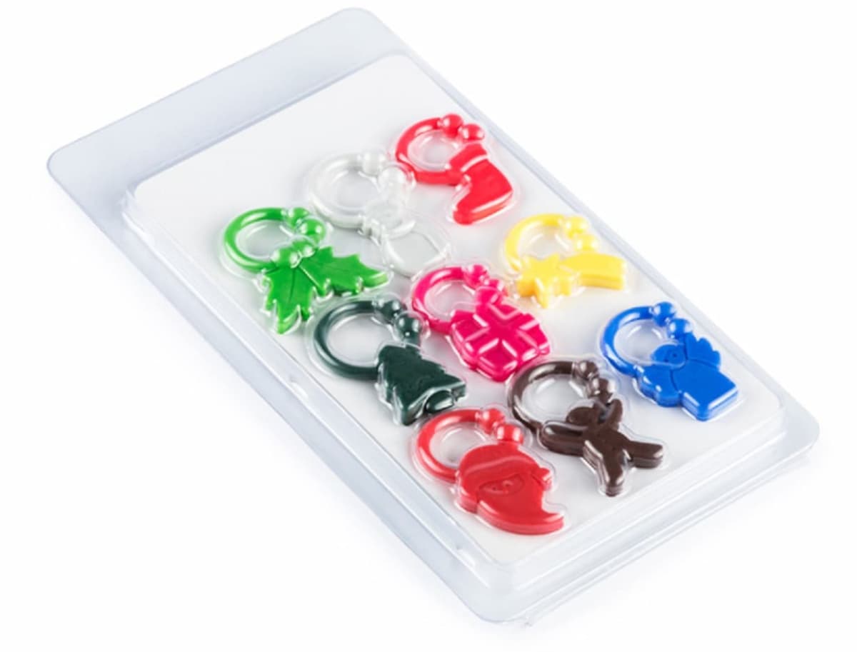 A clear plastic package contains eight colorful keychains shaped like various holiday icons, including trees, stockings, gifts, and reindeer. The keychains are arranged in two neat rows.