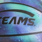 Close-up of a basketball with a textured surface and a vibrant blue and green galaxy pattern. The word TEAM is partially visible in bold black lettering across the ball.