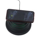 A smartphone with a maroon case is placed on a black wireless charging pad. The phone screen displays a charging icon with green light emanating from beneath the pad, indicating the device is charging.