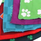 Colorful fabric squares layered, featuring various designs: a green square with white paw prints, a purple-edged square, a blue square with geometric patterns, and a red square with green clovers.
