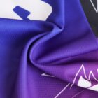 Close-up of a purple and black fabric with a smooth, shiny texture, featuring white abstract designs and folds.