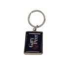 A rectangular keychain with a silver ring and border displays the text Gary Peer in white on a black background, accompanied by a small red logo.