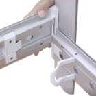 Close-up of a hand assembling two silver metal frames with white plastic connectors. The frames are aligned at a corner, showing the joining mechanism.