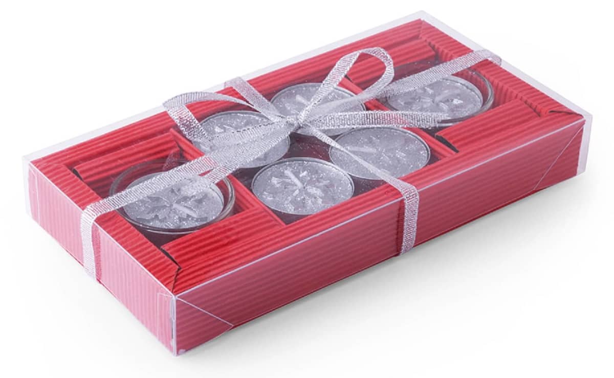 A rectangular gift box with a clear lid, containing six silver tealight candles arranged in pairs. The box is decorated with a shiny silver ribbon tied in a bow. The sides of the box are red with a striped texture.