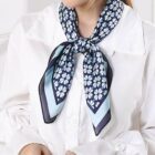 A person wearing a white blouse with a blue and white floral-patterned scarf tied in a bow around their neck.