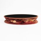 A circular brown serving tray with a smooth surface and a printed fabric strap wrapping around its outer edge, featuring a mix of brown and orange colors and abstract patterns. The tray is placed against a plain white background.