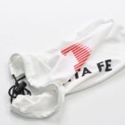 A white fabric drawstring bag with the text TA FE partially visible in black. A red, abstract design, possibly a half-circle or logo, is above the text. The bag is slightly wrinkled and laid on a white surface.