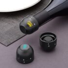 Close-up of a wine bottle with a black stopper labeled ART Prestige, and two similar black stoppers on a gray surface. One stopper has a digital readout displaying 8 on it, and a woven placemat is partially visible.