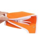 A hand holding an orange zippered pouch with white trim. The pouch is partially open, showing the white zipper and interior. The side features a small metal snap button. The fabric appears to be soft and flexible.