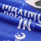 Close-up photo of a blue fabric with white text partially visible, including the words MAXIMU, potenti, and IN. A black and white soccer ball graphic is partially visible at the top right.