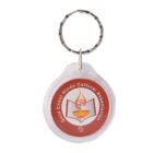A round keychain with a metal ring features the logo of the Gold Coast Hindu Cultural Association. The logo includes a lit lamp with a symbol above it, centered on an orange circular background.