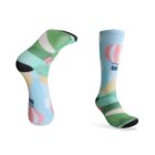 A pair of colorful socks featuring a pattern of hot air balloons in pastel colors like green, blue, and pink against a light blue background. One sock is upright, while the other is angled to show the design.