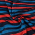 Close-up of a fabric with a swirling pattern of red, blue, and black diagonal stripes. The colors alternate, creating a dynamic and vibrant design, centered around a subtle twist in the fabric.