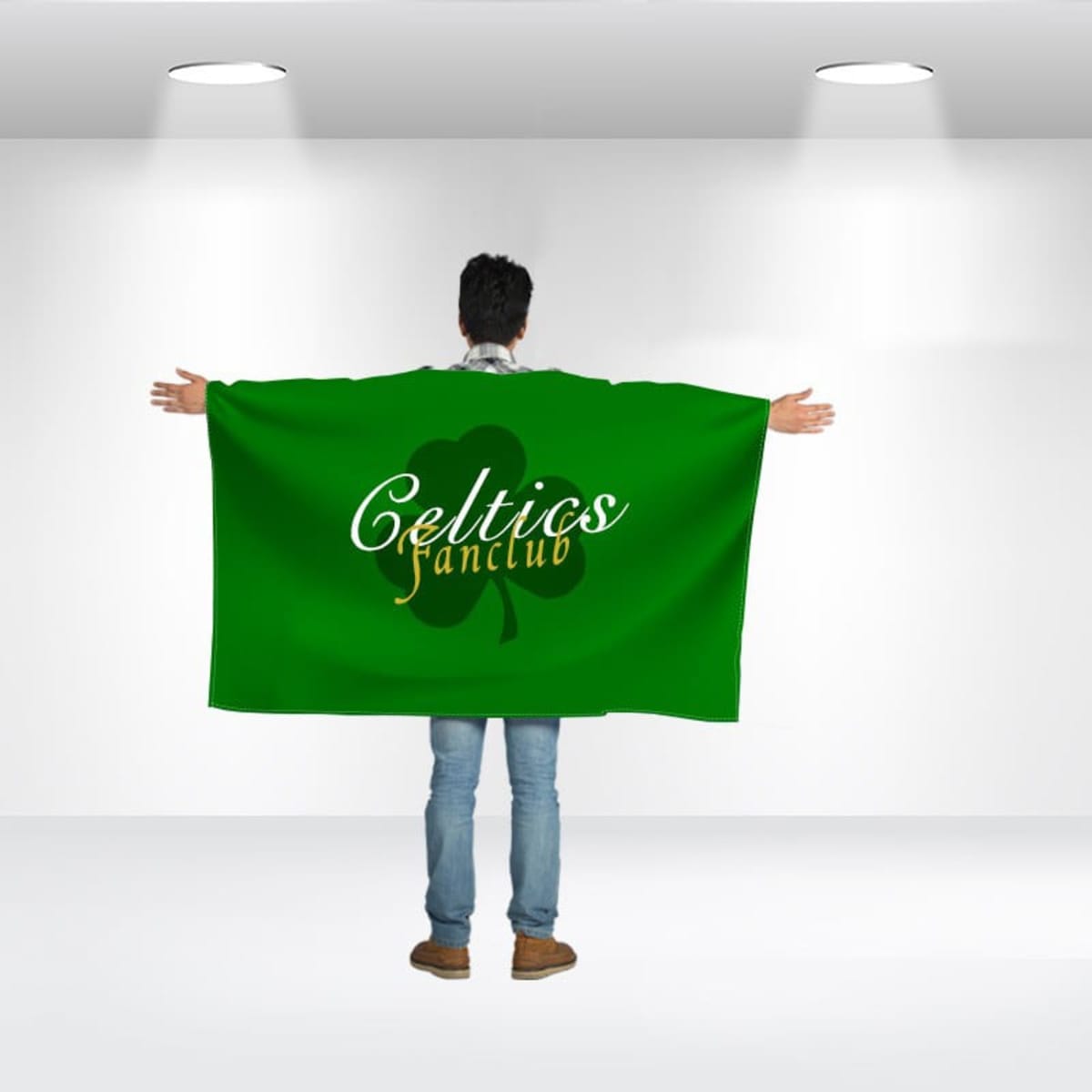 Person standing with their back to the camera, wearing a large green cloak with Celtics fanclub and a shamrock design printed on it. The room is well-lit with two overhead lights.