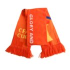 An orange sports scarf with fringed ends. The scarf displays the words GLORY AND in white text.