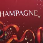 The image features a festive red background with the word CHAMPAGNE in elegant white letters. Decorative elements include sparkling accents and a red ribbon curving through the scene.